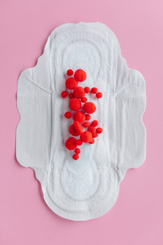 Artistic display of raspberries on a menstrual pad on a pink background, symbolizing menstruation.